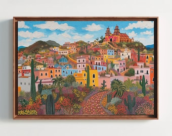May include: A framed landscape painting depicting a vibrant town nestled in hills under a blue sky with white clouds. The scene features colorful buildings, a prominent church, and a foreground filled with various cacti and desert flora.