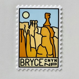 Puede incluir: Una pegatina blanca con una ilustración roja, naranja y amarilla de formaciones rocosas. La pegatina tiene un fondo de cielo azul con un sol blanco. El texto "BRYCE CANYN NP" está impreso en negro en la parte inferior de la pegatina.
