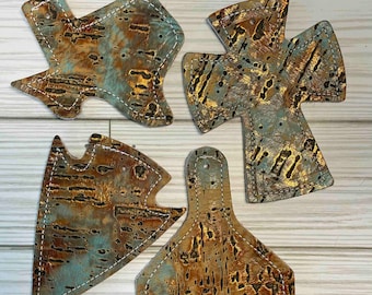 May include: Four leather coasters with a cork-like texture and a gold and teal color scheme. The coasters are shaped like a star, a cross, a triangle, and a rounded rectangle.