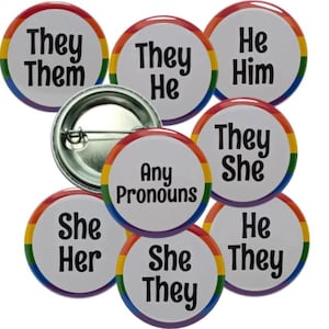 May include: A collection of round pronoun buttons with a rainbow border. The buttons display pronouns such as "They/Them", "He/Him", "She/Her", and "They/She". One button has the text "Any Pronouns".
