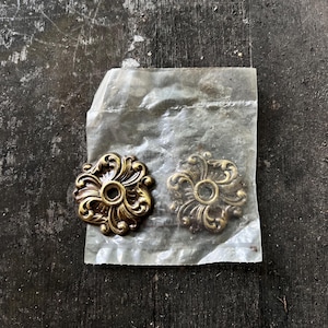 May include: Two gold-toned metal decorative accents with a floral design. The accents are packaged in a clear plastic bag.