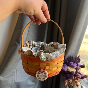 May include: A small, woven basket with a red and orange trim. The basket is lined with a floral fabric and has a tag that reads "Happy Mother's Day".