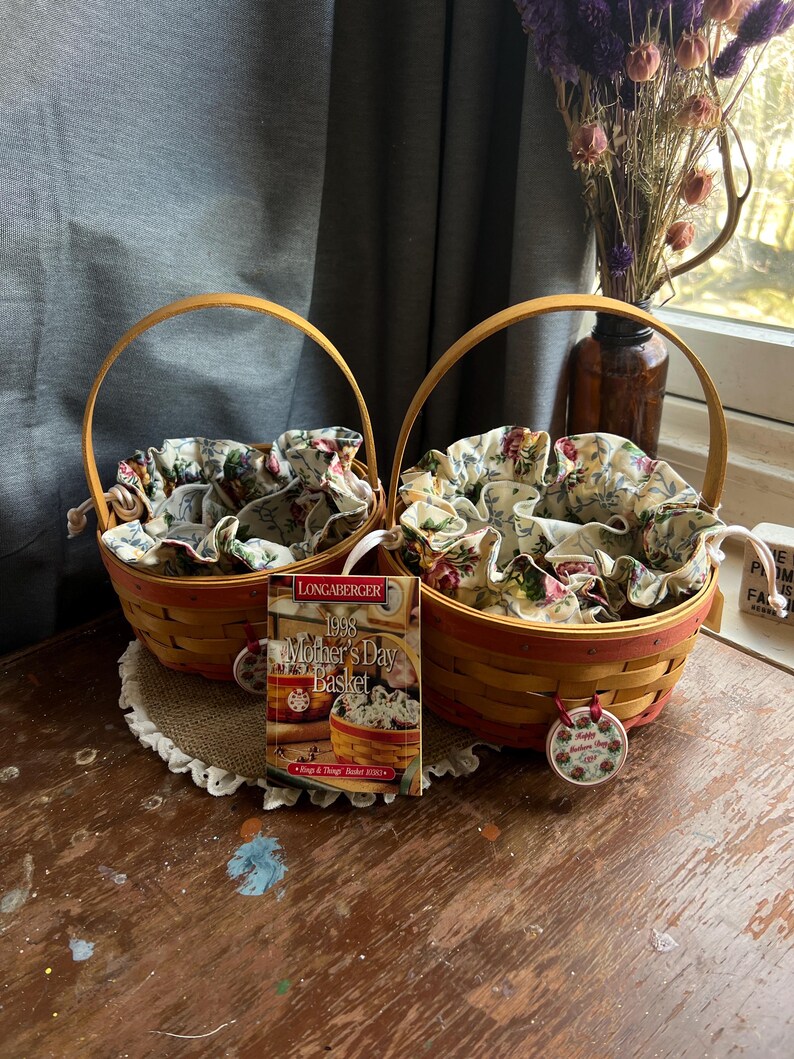 May include: Two Longaberger wicker baskets with floral fabric liners. The baskets are yellow and red with a brown wooden handle. A tag is attached to one basket that reads "1998 Mother's Day Basket".