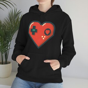 May include: Black hoodie with a red heart-shaped design featuring a stylized video game controller. The controller has a green plus sign, a red circle, and two black dots.
