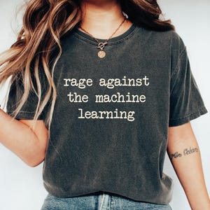 May include: A dark gray t-shirt with the text "rage against the machine learning" printed in white on the front.