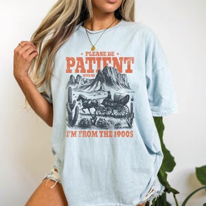 a woman wearing a shirt that says please be patient i'm from the mountains