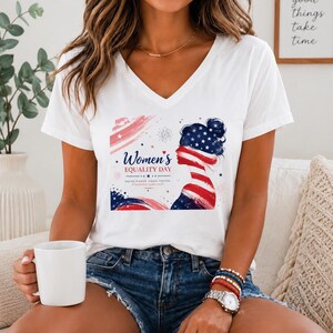 May include: A white V-neck t-shirt featuring a graphic print of a silhouette profile filled with American flag patterns. The text reads Women's EQUALITY DAY, EQUAL RIGHTS, EQUAL FUTURE, STRONGER TOGETHER, accompanied by red and blue brush strokes.