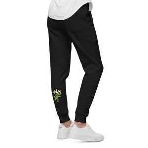 Può includere: Pantaloni della tuta neri con un disegno di fiori bianchi sulla gamba sinistra.