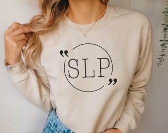 Puede incluir: Una sudadera beige con un círculo negro y el texto "SLP" dentro del círculo. El círculo está rodeado de comillas.