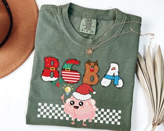 May include: Green t-shirt with a Christmas-themed design featuring the letters "BSBA" with festive decorations. A cartoon brain wearing a Santa hat is holding a lightbulb and standing on a checkered pattern.