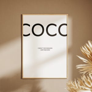 以下が含まれることがあります： 「COCO」の文字が大きく黒字で書かれたフレーム入りのアートプリント。下には「I DON'T DO FASHION I AM FASHION」の文字。明るい木製のフレームに入っており、ベージュの壁に掛けられている。