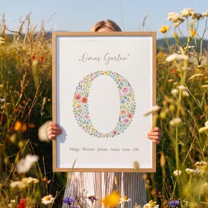 Könnte beinhalten: Ein gerahmter Druck mit dem Text Omas Garten oben und einem großen Buchstaben O, der aus einem bunten Blumenkranz aus rosa, gelben, blauen und grünen Blüten besteht. Die Namen Helga, Werner, Julian, Anna, Lina und Ole stehen unten.