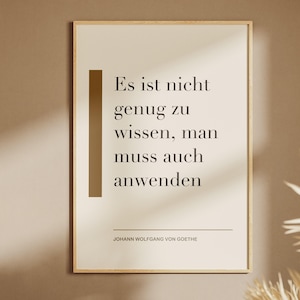 Könnte beinhalten: Ein rechteckiges Wandbild in einem hellen Holzrahmen mit cremefarbenem Hintergrund und schwarzem Text: Es ist nicht genug zu wissen, man muss auch anwenden. Links befindet sich ein vertikaler brauner Balken, unten steht der Name Johann Wolfgang von Goethe.