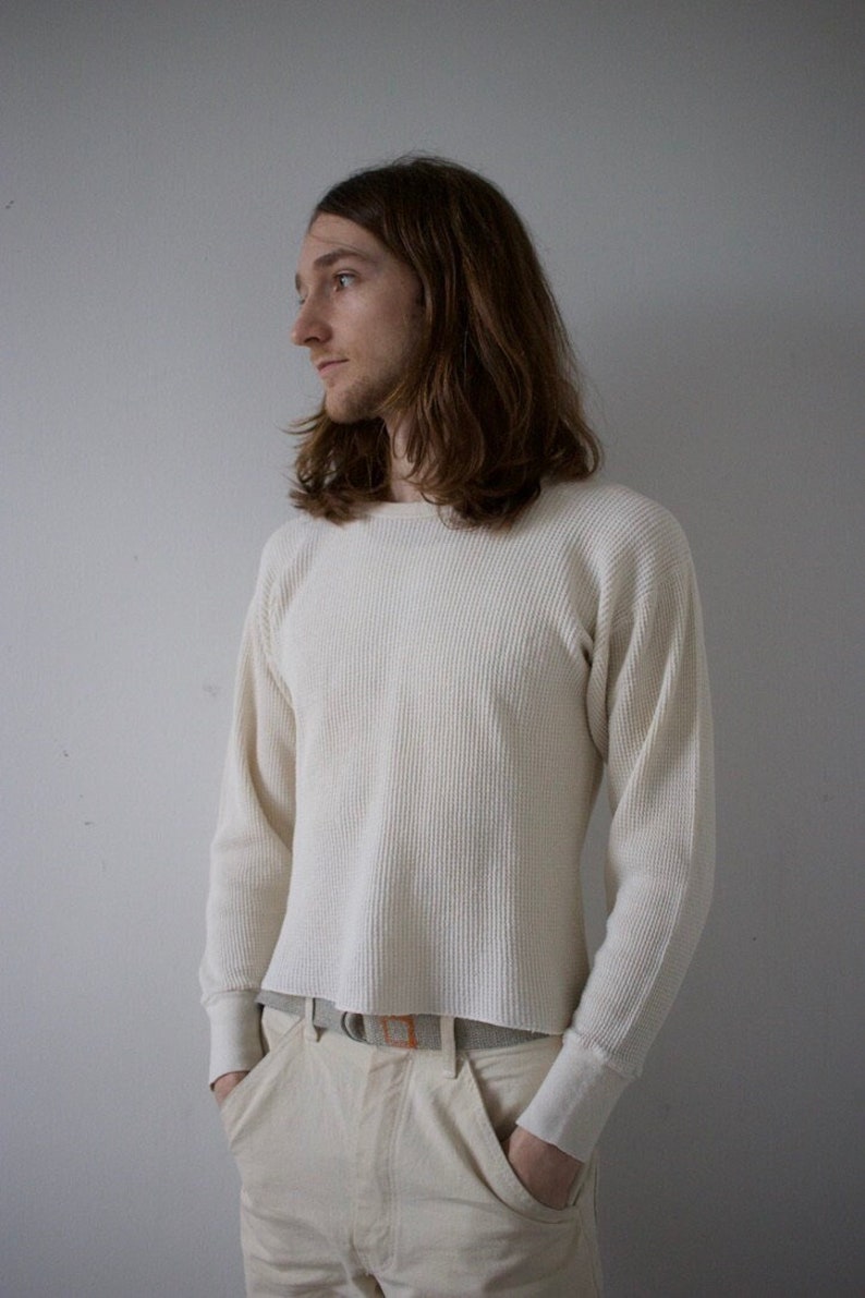 K&ouml;nnte beinhalten: Ein wei&szlig;es, lang&auml;rmeliges Thermoshirt mit gerippter Struktur. Das Shirt ist in eine wei&szlig;e Hose mit einem braunen G&uuml;rtel gesteckt.