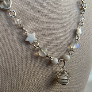 Puede incluir: Collar plateado con cuentas blancas, dijes en forma de estrella y un colgante de jaula de alambre. El collar incluye eslabones en forma de coraz&oacute;n y detalles de cristal transparente, creando un dise&ntilde;o delicado y caprichoso.