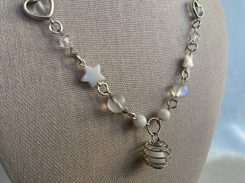 Puede incluir: Collar plateado con cuentas blancas, dijes en forma de estrella y un colgante de jaula de alambre. El collar incluye eslabones en forma de coraz&oacute;n y detalles de cristal transparente, creando un dise&ntilde;o delicado y caprichoso.
