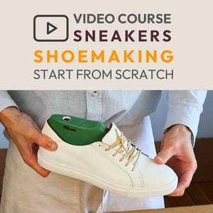 May include: White leather sneaker with beige laces and a green shoe last. The image includes text that reads "VIDEO COURSE SNEAKERS SHOEMAKING START FROM SCRATCH". The shoe is held by a person.