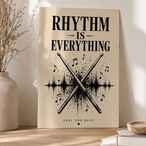 Może przedstawiać: Prostokątny wydruk ścienny na beżowym tle z czarnym napisem RHYTHM IS EVERYTHING. Poniżej tekstu znajdują się dwie skrzyżowane pałki perkusyjne na tle czarnej grafiki fali dźwiękowej, nuty oraz napis FEEL THE BEAT z małym sercem.