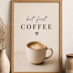 May include: A rectangular wooden frame containing a print with a beige background. The text reads but first, COFFEE above a small heart symbol. Below the text is a photographic image of a speckled ceramic mug filled with latte art.