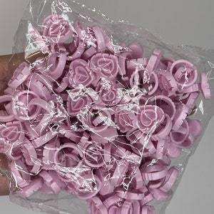 May include: A bag of pink plastic rings with a heart design. The rings are used for nail art and are designed to hold the nail in place while it dries.