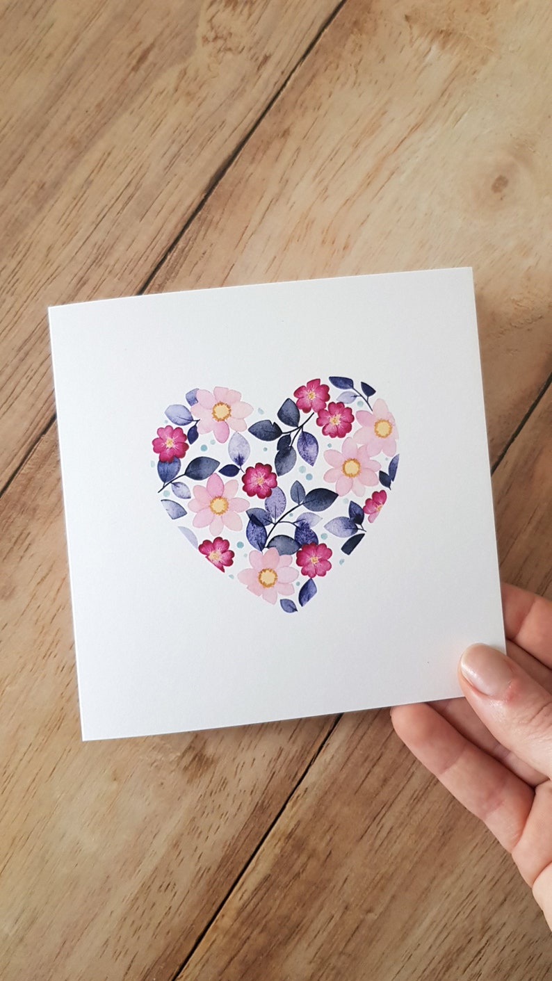 May include: A white card with a pink and purple floral heart design. The heart is made of pink and purple flowers with blue leaves and white dots.