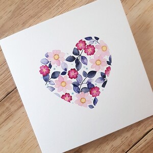 May include: A white card with a pink, purple, and blue floral heart design.