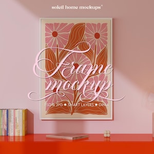 Peut inclure: Une affiche encadrée avec un motif floral sur fond crème, représentant des fleurs roses et des feuilles couleur rouille. Le cadre est blanc, et le texte "Frame mockup" est superposé. L'image est affichée sur un mur rose.