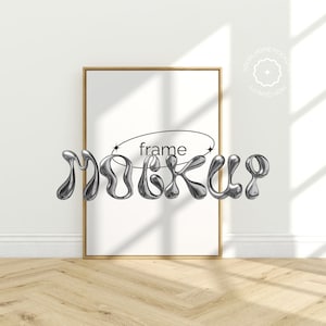 Könnte beinhalten: Ein weißer Rahmen-Mockup mit einem Holzrahmen, der auf einem hellen Holzboden steht. Das Wort "frame" ist in schwarzer Schrift im Rahmen geschrieben. Das Wort "mockup" ist in einer silbernen, 3D-artigen, flüssigen Schriftart vor dem Rahmen geschrieben.