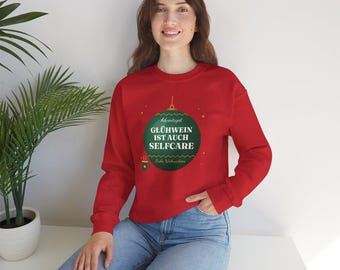May include: A red long-sleeve sweatshirt featuring a dark green Christmas ornament graphic on the chest. The ornament contains the white text "GLÜHWEIN IST AUCH SELFCARE" and "Frohe Weihnachten" with a small mug icon below it.