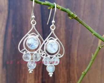 May include: A pair of silver dangle earrings with moonstone gemstones. The earrings feature a delicate, intricate design with multiple round stones.