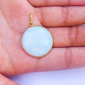 May include: A round white opal pendant with a gold setting. The pendant is on a white background.