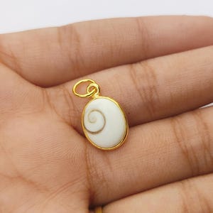 May include: Gold oval pendant featuring a white seashell with a brown spiral inside.
