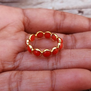 May include: A gold ring with a band of small, round, red coral stones.