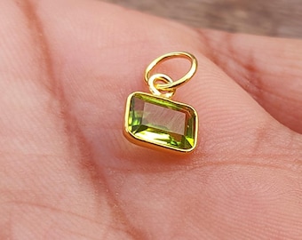 May include: A gold pendant with a green gemstone. The gemstone is a rectangular shape with a smooth, polished surface.