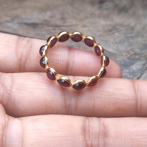 Könnte beinhalten: Ein goldener Ring mit einer Reihe kleiner, runder, roter Edelsteine.