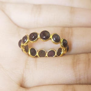 May include: A gold ring with a band of dark purple gemstones. The ring is on a person's finger.