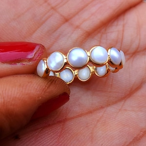May include: A gold ring with a row of white pearl-like stones.