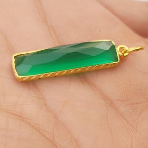 Könnte beinhalten: Ein goldener Anhänger mit einem grünen Edelstein. Der Edelstein ist rechteckig und hat einen facettierten Schliff. Der Anhänger hat ein schlichtes Design und ist perfekt, um jedem Outfit einen Hauch von Eleganz zu verleihen.