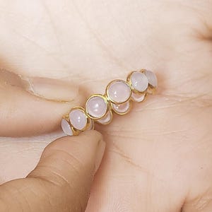 May include: A gold ring with a row of pale pink round stones.