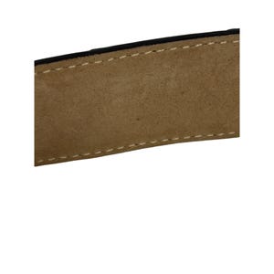 Puede incluir: Primer plano de una secci&oacute;n de un cintur&oacute;n de cuero. El cintur&oacute;n es de color marr&oacute;n claro con un borde negro y costuras blancas. El cuero tiene un aspecto texturizado.