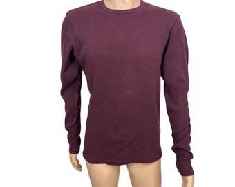 May include: A long-sleeved, burgundy-colored thermal shirt. The shirt has a ribbed texture and a crew neck. The sleeves are long and fitted, and the overall style is casual and comfortable. The shirt is displayed on a mannequin.