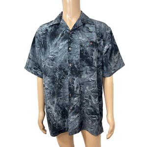 May include: A short-sleeved button-down shirt with a black and gray tie-dye pattern. The shirt has a collared neckline and a single chest pocket.