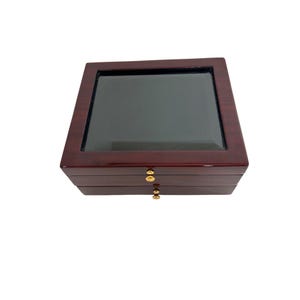 May include: A mahogany wood jewelry box with a glass top and three drawers. The box has gold-colored knobs.