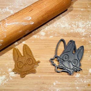 Könnte beinhalten: Zwei Ausstecher, einer ist eine schwarze Katze und der andere eine braune Katze. Beide befinden sich auf einer Holzoberfläche mit verstreutem Mehl.