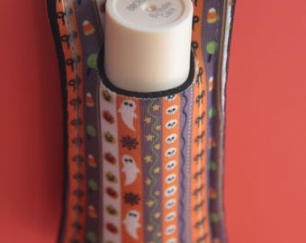 Könnte beinhalten: Ein Halloween-Lippenbalsamhalter mit einem Metall-Schlüsselring. Der Halter hat ein farbenfrohes Muster aus Geistern, Kürbissen und Zuckermais auf orangefarbenen, lila und weißen Streifen. Der Lippenbalsam ist mit "Birthday Cake" beschriftet.