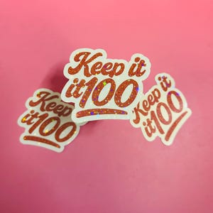 Può includere: Tre adesivi con la frase "Keep it 100" in un carattere arancione glitterato. Gli adesivi hanno un bordo bianco e sono disposti su uno sfondo rosa. Gli adesivi sono un design divertente e accattivante.