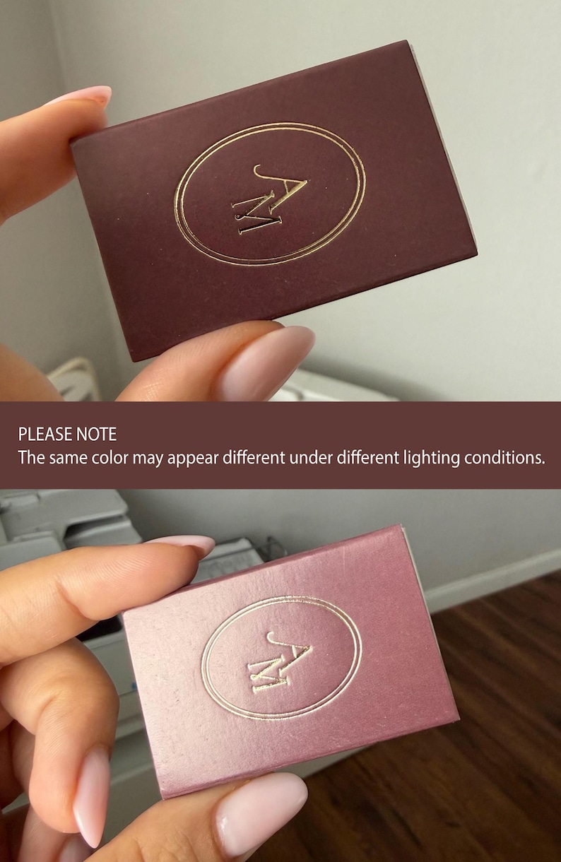 May include: A rectangular box with a matte finish featuring a gold foil embossed oval frame and the letters AM in the center. The box is shown in two different shades, one a deep dark brown and the other a lighter mauve, to demonstrate color variation.