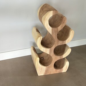 May include: A wooden wine rack with a unique, organic design. The rack has six bottle slots and is made of natural wood with a light brown finish.