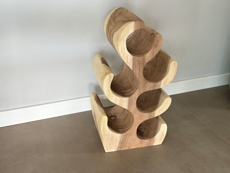 May include: A wooden wine rack with a unique, organic design. The rack has six bottle slots and is made of natural wood with a light brown finish.