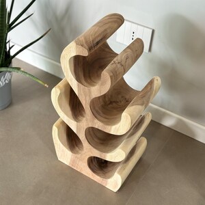 May include: A wooden wine rack with a unique, organic design. The rack is made of natural wood and has a light brown color. It features multiple curved shelves that can hold up to 6 bottles of wine.